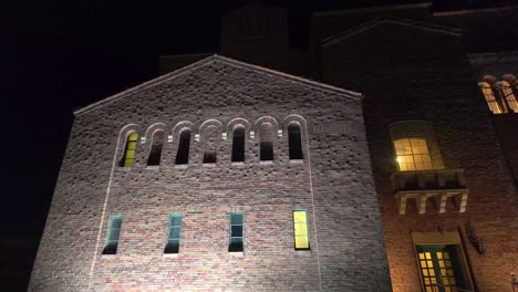 Footage-looking-up-at-illuminated-vintage-brick-building-with-rows-of-arched-windows-glowing-yellow-from-within-at-night