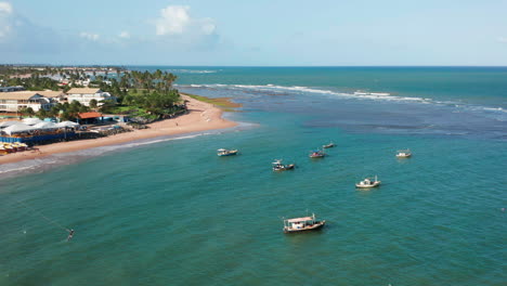 Vista-Aérea-De-Una-Persona-Practicando-Kitesurf,-Algunos-Barcos-Estacionados-Y-Grandes-Palmeras-Al-Fondo,-Guarajuba,-Bahía,-Brasil.