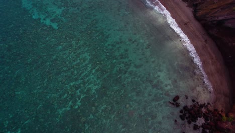 Impresionante-Vista-Aérea-Del-Exótico-Destino-Tropical-Hawaiano-Con-Una-Tranquila-Superficie-Turquesa-Del-Océano,-Arrecifes-De-Coral-Y-Acantilados-De-Tierra-Roja