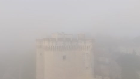 Scenic-aerial-view-through-thick-foggy-clouds-with-medieval-fortress-in-Avignon,-France