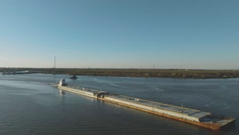 A-stunning-aerial-view-captures-a-tugboat-navigating-the-Houston-Ship-Channel,-pushing-a-barge-at-dusk-in-Houston,-Texas