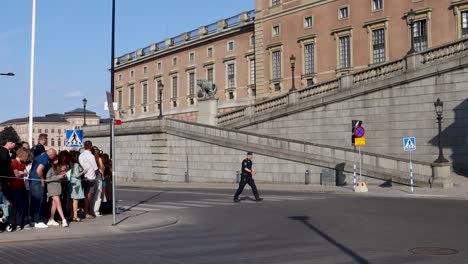 Excited-patriotic-citizens-wait-outside-of-Swedish-Royal-Palace-as-Officer-Guard-walks-in-empty-street,-Stockholm-Sweden