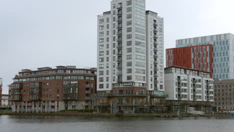 Modernos-Apartamentos-Frente-Al-Mar-En-Los-Muelles-De-Dublín-Bajo-Un-Cielo-Nublado,-Durante-El-Día,-Vida-Urbana-Junto-Al-Río