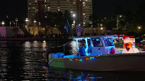 Menschen-Auf-Einem-Boot-Mit-Hellen-Und-Bunten-Lichtern-Und-Wehenden-Flaggen-In-Einer-Weihnachtsbootsparade,-Statische-Aufnahme