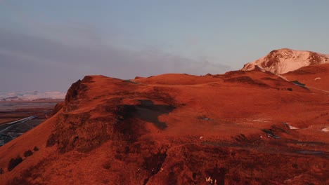 Cinematic-drone-shot-showing-red-lighting-mountains-with-snow-on-peak-at-golden-sunset