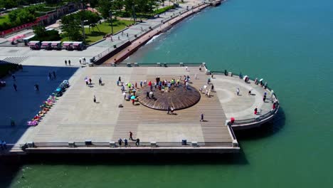 Aerial-forward-dolly-plus-tilt-down-panoramic-view-of-Weihai-Xingfu-park-wharf-with-tourists-standing-on-ancient-scribed-mini-dome