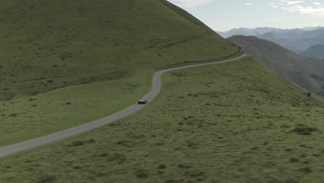 Racing-vintage-car-driving-along-panoramic-road-of-Col-Inharpu-with-mountain-range-in-background,-Basque-Pyrenees,-France