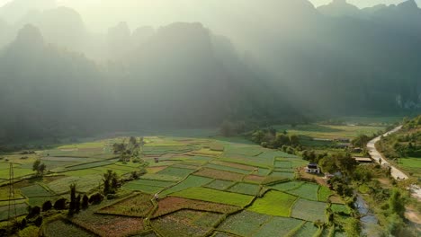 Mystic-fertile-valley-and-patchwork-crops,-soft-evening-sun-rays-through-mountainous-limestone-formations-on-the-horizon