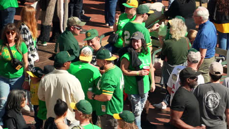 Crowd-of-baseball-fans-in-green-SELL-shirts-enjoying-Athletics-Fan-Fest,-sunny-day