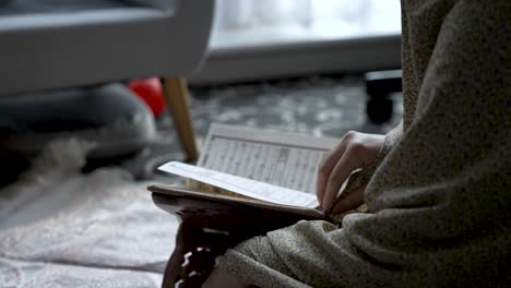 Person-reading-Quran-in-a-dimly-lit-room,-focus-on-text-and-hands,-cozy-atmosphere