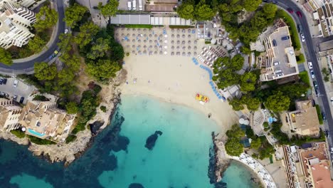 Drone-descending-while-making-a-slow-orbit-over-the-beachfront-of-Playa-Lletas,-a-resort-in-the-island-of-Mallorca-in-Spain