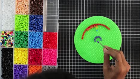 Colorful-beads-on-pegboard-for-craft-activity,-hand-creating-a-pattern,-timelapse