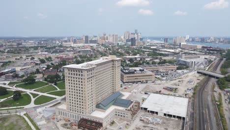 Toma-Aérea-Lateral-Desde-La-Estación-Central-De-Michigan-En-Un-Día-Agradable-Con-Vías-De-Tren-Y-Un-Parque-Local-Enfrente