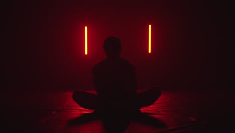 silhouette-of-a-person-stretching-while-sitting-in-lotus-position-in-dark-red-room