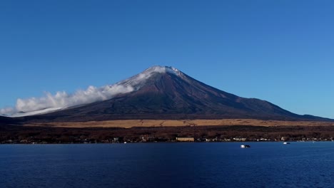 Majestic-Mount-Fuji-with-snow-cap-overlooking-blue-lake,-clear-sky