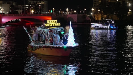 Feliz-Cartel-De-Swiftmas-Iluminado-Mientras-La-Familia-Baila-En-Un-Barco-Por-La-Noche-Durante-El-Desfile-De-Navidad
