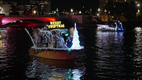 Frohe-Swiftmas-Zeichen-Beleuchtet,-Wie-Die-Familie-Tanzt-Auf-Dem-Boot-In-Der-Nacht-Während-Der-Weihnachtsparade