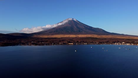 Mount-Fuji-seen-across-a-calm-lake-with-boats-at-dawn,-clear-blue-sky