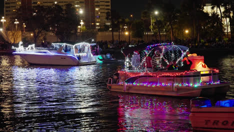 Pontonboote-Und-Schnellboote,-Behangen-In-Leuchtenden-Rot-blau-violetten-Weihnachtslichtern,-Ziehen-Auf-Dem-Wasser-Entlang