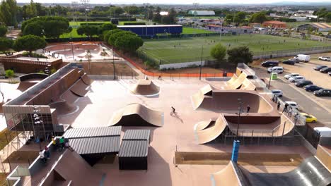 Aerial-revealing-shot-of-people-using-a-skatepark-and-a-football-field