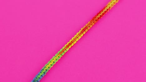 Primer-Plano-De-Una-Colorida-Y-Vibrante-Pulsera-De-Macramé-Roscada-Con-Un-Patrón-De-Colores-Del-Arco-Iris,-Descansando-Sobre-Un-Fondo-Rosa-Neón