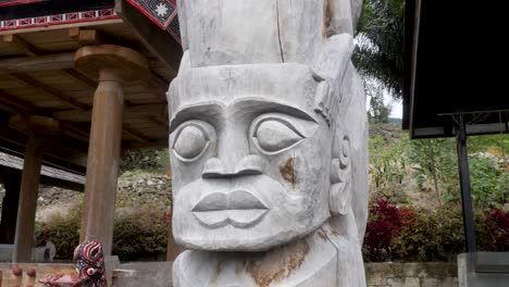Carved-Toba-Batak-totem-pole-on-Samosir-Island,-vibrant-flora-background,-cultural-artifact