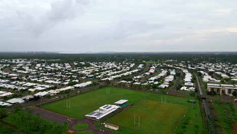 Drone-Aéreo-De-Un-Suburbio-Residencial-Con-Múltiples-óvalos-De-Rugby-En-Un-Día-Lluvioso,-Vista-Panorámica-De-Techos-Blancos-Homogéneos-En-Calles-Curvas