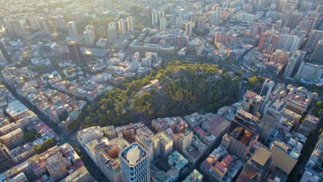 Cerro-Santa-Lucía-Al-Amanecer,-Luz-Dorada-Del-Sol-Bañando-El-Paisaje-Urbano,-Vista-Aérea