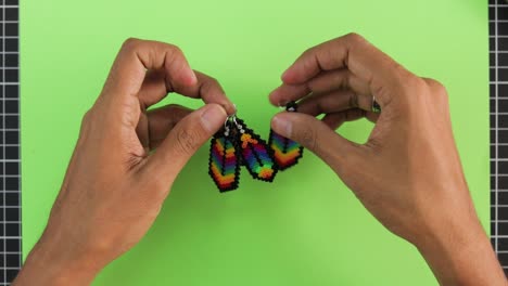 Hands-crafting-colorful-bead-earrings-on-a-green-background,-detailed-and-vibrant