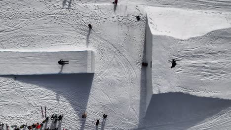 Aerial-top-down-view-of-snowy-ramp,-skiers-jump-and-perform-tricks,-Czechia
