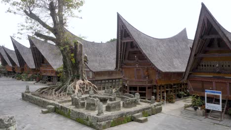 Traditional-Batak-houses-with-soaring-roofs-at-Samosir-Island,-Lake-Toba,-with-the-ancient-Batu-Parsidangan-stones-in-the-foreground