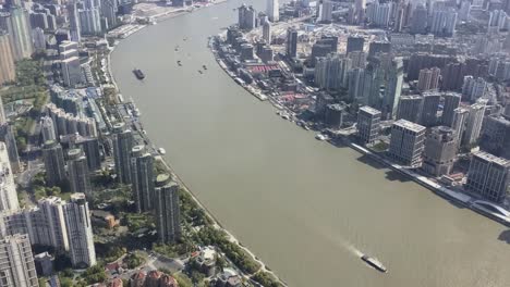 Ships-transporting-goods-and-material-on-Huangpu-river-in-Shanghai,-China,-top-view-with-vertical-panning