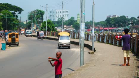 Indian-Boy-Flying-Kite-On-The-Street-With-Vehicles-Passing-By