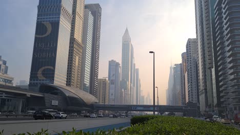 Traffic-in-Downtown-Dubai-UAE,-Air-Pollution-Above-Skyscrapers-and-Emirates-Towers-Metro-Station