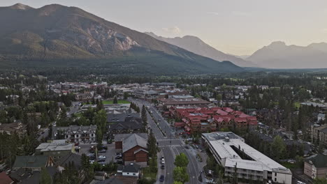 Banff-AB-Canada-Aerial-v1-fly-along-the-avenue-across-the-town-towards-Bow-river-capturing-quaint-townscape,-forested-valleys-and-mountain-ranges-at-sunset---Shot-with-Mavic-3-Pro-Cine---July-2023