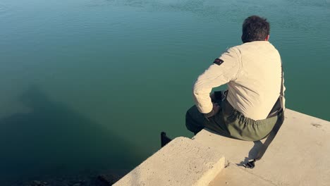 Capturing-a-fisherman-seated-on-the-water's-edge-platform,-peacefully-observing-and-resting,-embodying-the-essence-of-a-quaint-fishing-village