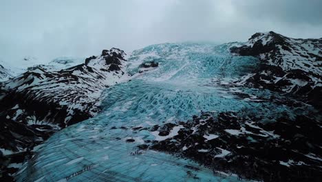 Aerial-Drone-View-Of-People-Hiking-On-Blue-Glacier-Field-In-Iceland,-Land-of-Fire-and-Ice