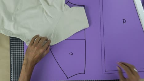 Man-drawing-on-a-purple-cardboard-the-outline-of-clothing