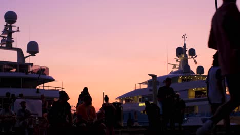 Close-Up-View-of-Player-Silhouettes-During-Street-Soccer-Tournament-at-Sunset-with-Yachts---Spectators-in-Background