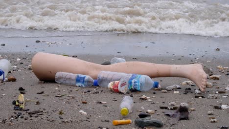 Broken-off-leg-from-clothes-mannequin-drifted-ashore-with-plastic-water-bottles-and-other-rubbish-trash-polluting-beach-of-tropical-island-after-heavy-storm