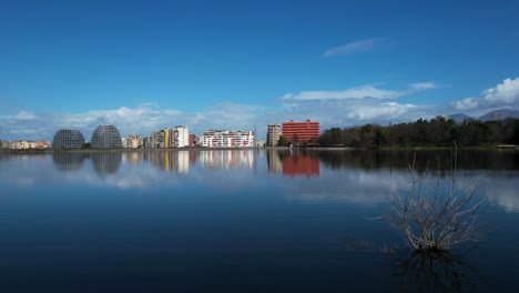 Lakeside-Serenity:-Relaxing-by-Tirana's-Lake,-Where-Calm-Waters-Mirror-the-Blue-Sky-and-Architectural-Buildings