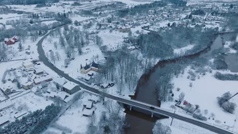Abava-river-curving-through-snowy-Renda-village-,-winter-scenery,-aerial-view