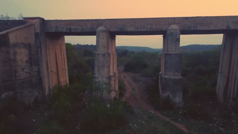 Luftaufnahme-Einer-Alten-Eisenbahnbrücke-Aus-Beton-Mit-Gleisen-Und-Dichten-Waldhügeln-Im-Hintergrund-Während-Der-Späten-Abendzeit-Per-Drohne