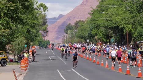 Toma-En-Cámara-Lenta-De-Ciclistas-Al-Frente-Y-Corredores-Al-Fondo-En-El-Ironman-70-De-Salud-Entre-Montañas