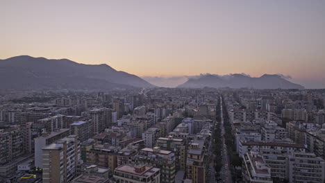 Palermo-Italia-Toma-De-Seguimiento-Aérea-V7-Sobrevuelo-Del-Centro-De-La-Ciudad-Capturando-El-Paisaje-Urbano-Al-Atardecer,-El-Tráfico-Callejero-Y-El-Paisaje-Montañoso-En-El-Horizonte---Filmado-Con-Cine-Mavic-3---Mayo-De-2023