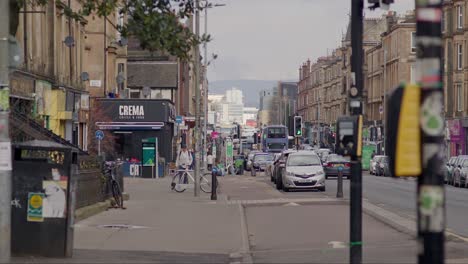 People-walking-up-Victoria-Road,-cars-passing-the-frame-with-Glasgow-city-center-in-the-distance