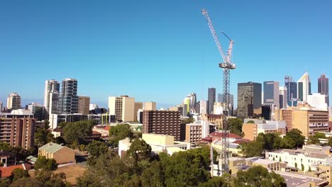 Aerial-pull-back-shot-of-tower-crane-moving-on-construction-site-with-flock-of-birds-flying-over-treetops