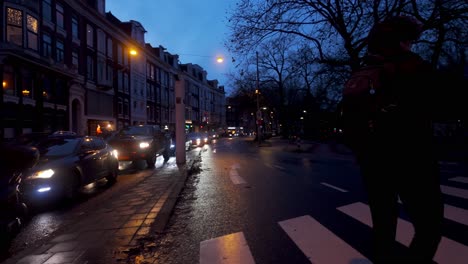 Night-time-view-of-busy-car-traffic-and-pedestrians-crossing-alongside-streets-of-Amsterdam,-Netherlands