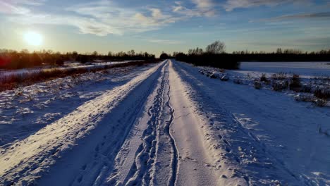 A-snow-covered-road-stretches-into-the-distance,-with-a-clear-blue-sky-and-long-shadows-cast-by-the-setting-sun