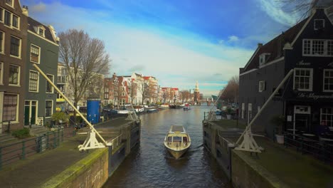 Canal-cruise-boat-sails-in-Amsterdam-river-next-to-famous-Sluyswacht-house